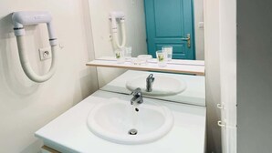 Un baño con un lavabo blanco, un espejo con iluminación, una puerta azul y un secador de pelo en la pared.
