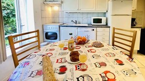 Una cocina con armarios blancos, estufa, microondas y una mesa de comedor con mantel colorido.