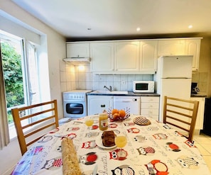 A kitchen with white cabinets, a stove, a microwave, and a dining table with a colorful tablecloth.