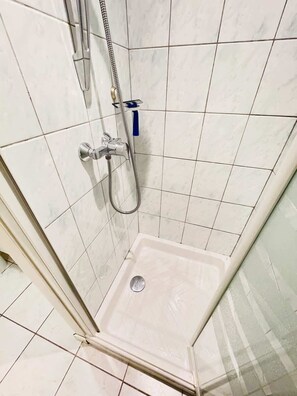 A shower with a handheld showerhead, a wall-mounted faucet, and a drain.