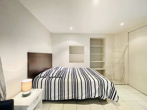 A modern bedroom with a bed, bedside lamp, and built-in shelving.