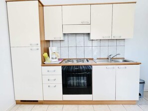 A compact kitchen with white cabinets, a built-in dishwasher, a stove, and a sink.