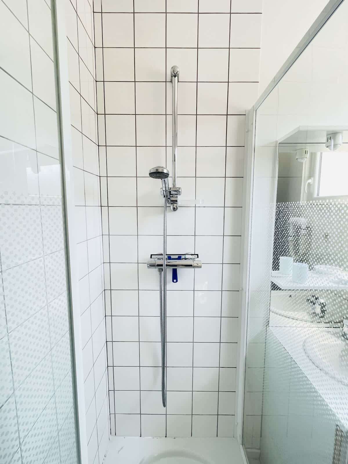 A modern bathroom with white tiled walls, a glass shower enclosure, and a visible toilet.