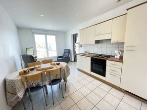 A compact kitchen with white cabinets, a dining table with chairs, and a large window.