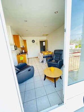 A compact living space with a kitchenette, a dining area with a table and chairs, a sofa, and a glass door leading to an outdoor area.