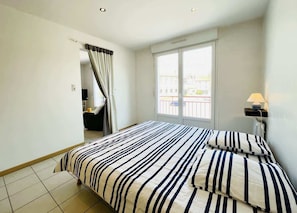 A hotel room with a bed, a window with a view, a lamp, and a door leading to another room.