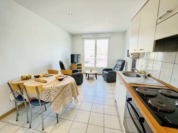 A modern kitchen with a dining area, a TV, and a large window.