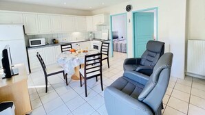 A modern kitchen with white cabinets, a dining table with chairs, a sofa, and a teal door. - Pasteur (Bains-les-Bains)