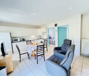 A modern kitchen with white cabinets, a dining table with chairs, a sofa, and a teal door.