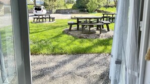 A view through a door into a grassy outdoor area with picnic tables and a white vehicle parked nearby. - Pasteur (Bains-les-Bains)