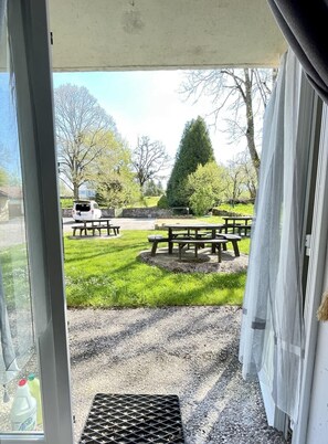 A view through a door into a grassy outdoor area with picnic tables and a white vehicle parked nearby.