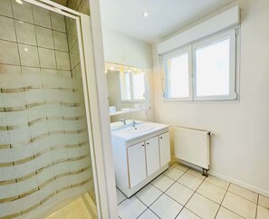 A bathroom with a shower, a sink, a mirror, and a window.