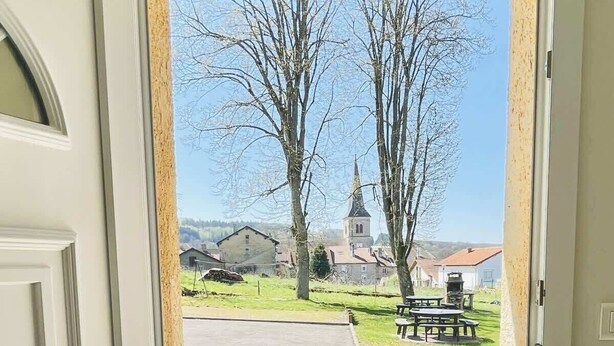 A door leading to a balcony with a view of a church and a park. - Athos (Bains-les-Bains)