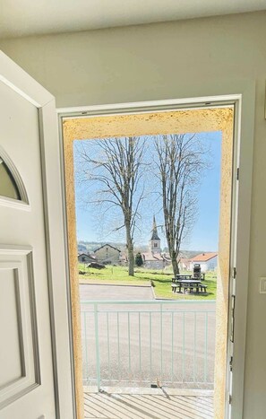 Puerta que da a un balcón con vistas a una iglesia y un parque.
