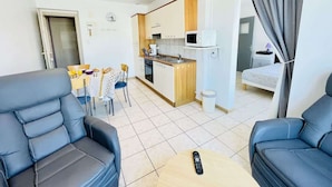 A modern living room with two leather sofas, a dining table with chairs, a kitchen area, and a small balcony with a curtain.