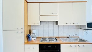 A compact kitchen with white cabinets, a built-in oven, a stovetop, and a sink.