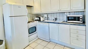 A kitchen with white cabinets, a refrigerator, an oven, a dishwasher, a microwave, and a coffee maker. - Porthos (Bains-les-Bains)