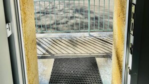 A view through a door with a yellow textured wall, a metal railing, and a clear sky. - Porthos (Bains-les-Bains)