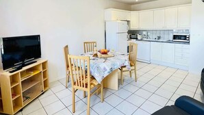 A compact living space with a dining area, kitchen, and a television on a stand. - Porthos (Bains-les-Bains)