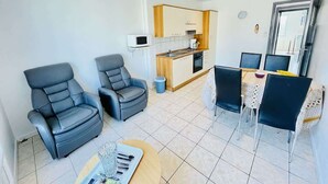 A modern living room with two leather sofas, a dining table with chairs, a kitchen area with a microwave, and a small trash bin. - Jacques Prévert (Bains-les-Bains)