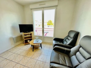 A living room with a TV, a sofa, a small table, and a balcony with a railing.