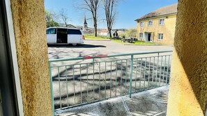 Une vue à travers la fenêtre d’un bâtiment, avec un fourgon blanc garé à l’extérieur, une rambarde en métal et un ciel dégagé.