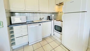 Une cuisine compacte avec des meubles blancs, un four à micro-ondes, un lave-vaisselle, un four et un réfrigérateur.