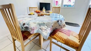 Un coin repas comprenant une table ronde, quatre chaises en bois, un téléviseur et une fenêtre avec des rideaux.