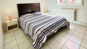 Une chambre à coucher avec un lit, des tables de chevet, une fenêtre avec des rideaux et un radiateur.