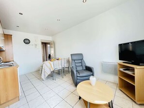 A living room with a TV, a sofa, a dining table with chairs, and a kitchen area with a refrigerator.