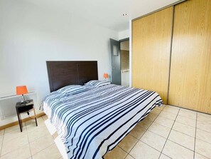 A bedroom with a bed, a nightstand, a lamp, a radiator, and a wooden wardrobe.