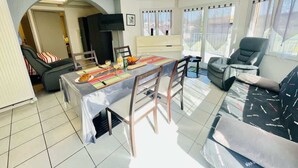 A spacious living area with a dining table, chairs, a sofa, a massage chair, and a TV.