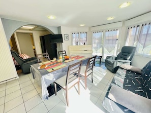 Un grand espace de vie comprenant une table à manger, des chaises, un canapé, un fauteuil massant et un téléviseur.