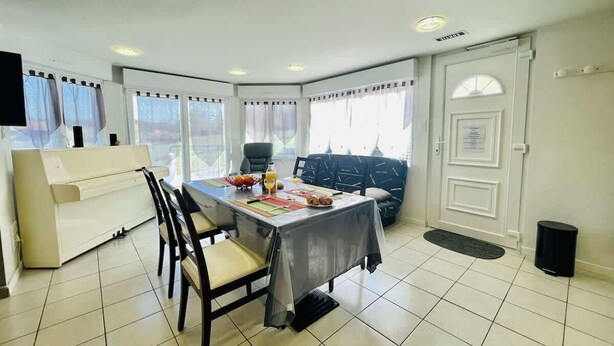 A dining area with a table set for two, a sofa, and a piano.