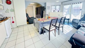 A modern kitchen with a dining area, a view of the outdoors, and a living room with a sofa and a TV.