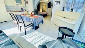A dining area with a table set for two, a kitchen in the background, and a piano.
