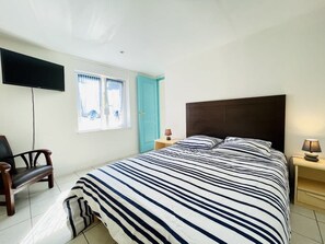 Ein Schlafzimmer mit Bett, Sessel, Fernseher und Fenster.