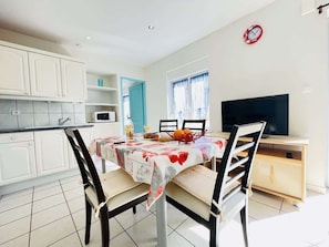 A dining area with a table set for two, a television, and a kitchen in the background.