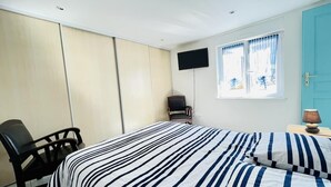 A bedroom with a bed, a chair, a TV, and a window with curtains. - Louis 11 (Bains-les-Bains)