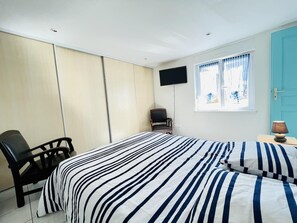 A bedroom with a bed, a chair, a TV, and a window with curtains.