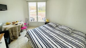 A bedroom with a bed, a desk, a chair, a table with breakfast, and a balcony with chairs.