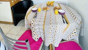 A compact kitchen with a microwave, a dining table with a patterned tablecloth, a clock, and a flat-screen TV on the wall.