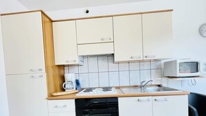 A compact kitchen with white cabinets, a black dishwasher, a microwave, and a wooden countertop.