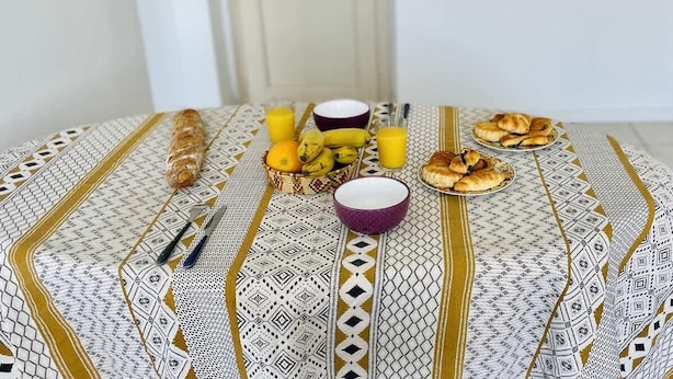 Une table avec des aliments pour le petit-déjeuner, notamment du pain, des bananes, des oranges, un bol et un verre de jus.