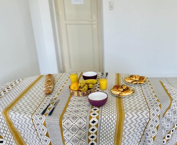 A table with breakfast items including bread, bananas, oranges, a bowl, and a glass of juice.