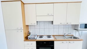 Une cuisine de taille réduite avec des meubles blancs, une cuisinière, un four et un évier.