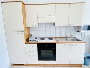 Eine kleine Küche mit weißen Schränken, einem Herd, einem Backofen und einer Spüle.