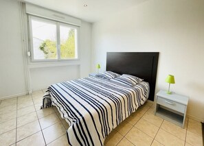 A bedroom with a bed, a nightstand, a window, and a view of greenery outside.