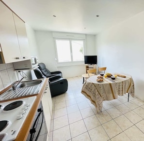 A modern kitchen with a stove, sink, and microwave, a dining area with a table set for two, and a TV in the background.
