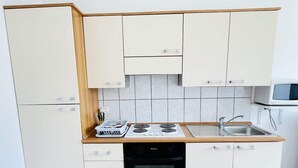 A compact kitchen with a stove, oven, sink, and white cabinets. - Rimbaud (Bains-les-Bains)